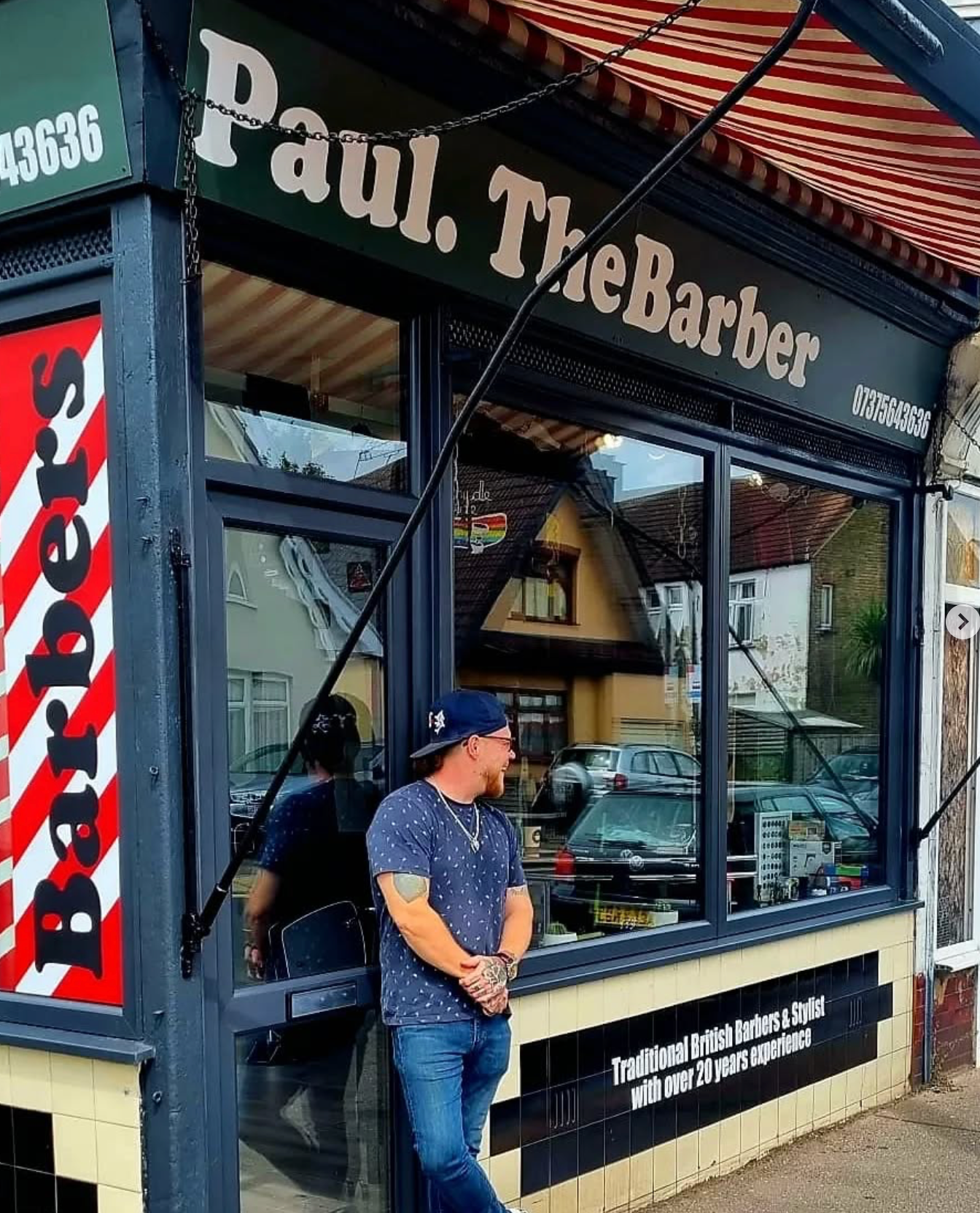 Paul The Barber, the owner of To The Bone clothing brand, posing outside his traditional barber shop in Westcliff-on-Sea, Essex, known for offering over 20 years of experience in barbering and styling.